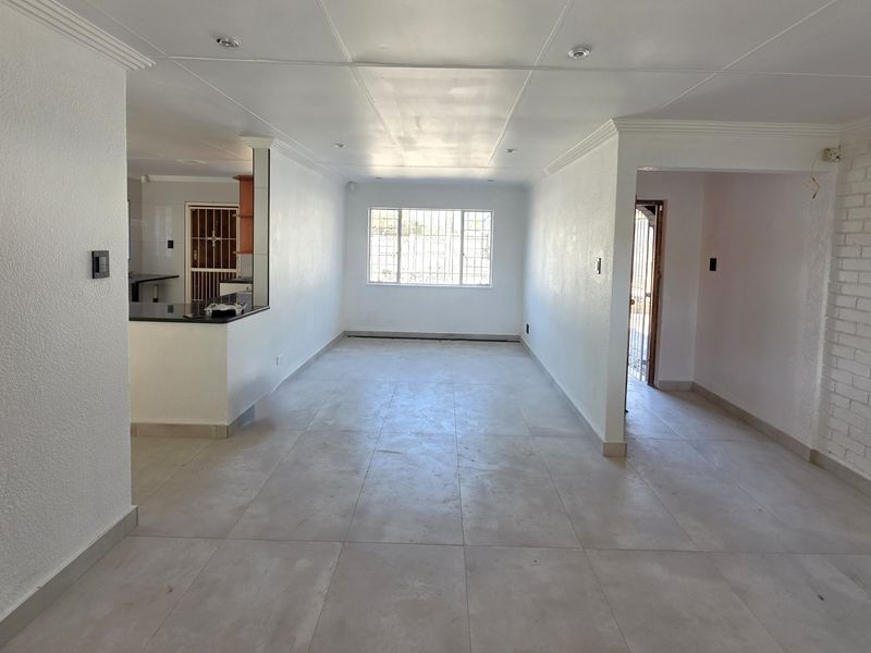 Spacious open-plan living area featuring neutral tiled flooring, recessed lighting, and an exposed brick feature wall, offering a bright and versatile layout.