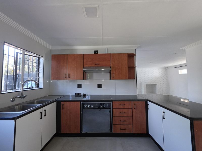 A clean, functional kitchen featuring two-tone cabinetry, granite countertops, built-in oven with hob, extractor fan, and a double sink with security bars on the window.