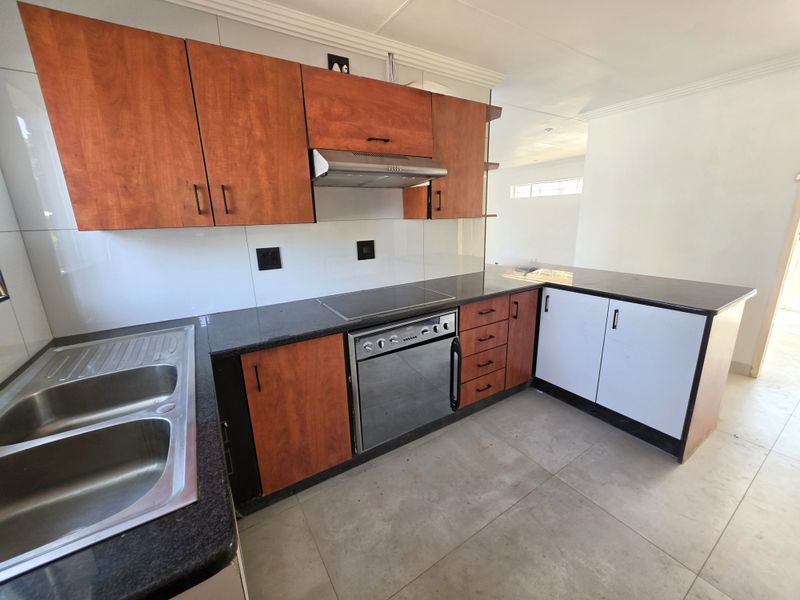 A clean, functional kitchen featuring wood-tone and white cabinetry, granite countertops, a built-in oven, electric hob, and a stainless steel double sink.