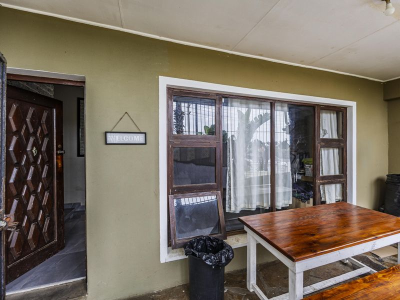 A covered patio area featuring a timber front door, security gate, and timber-framed windows with security bars, showing signs of wear and maintenance needs.