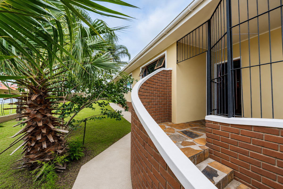 Rear exterior view featuring a curved brick wall, stone-paved steps, and a secure entrance gate leading to the garden area.