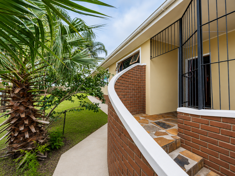 Rear exterior view featuring a curved brick wall, stone-paved steps, and a secure entrance gate leading to the garden area.
