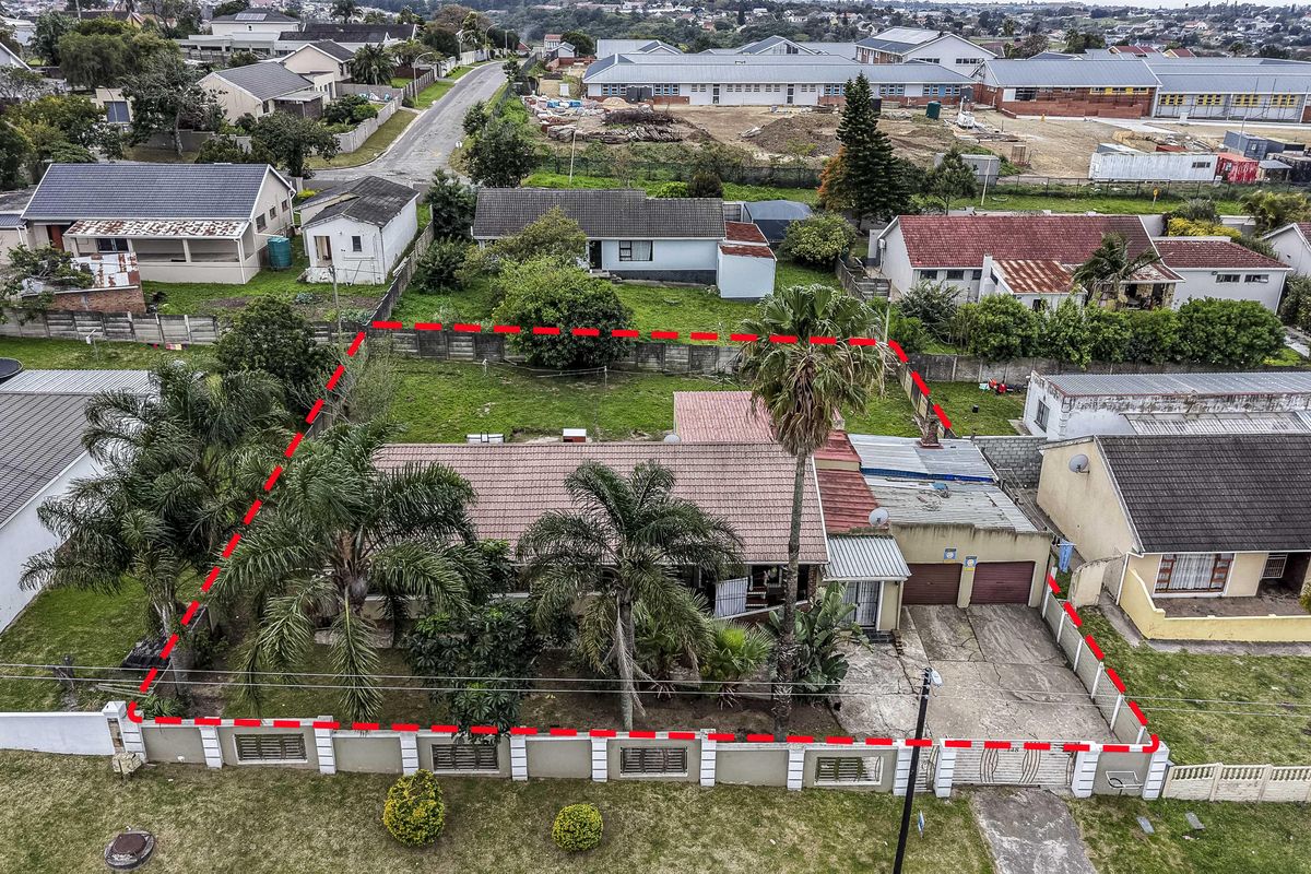 Aerial view of a residential property featuring a tiled roof, double garage, concrete driveway, and established garden within a fenced perimeter.