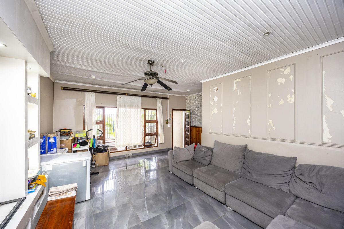 Living room featuring large format floor tiles, a ceiling fan, and timber-look ceiling panels, currently requiring cosmetic wall repairs and repainting.