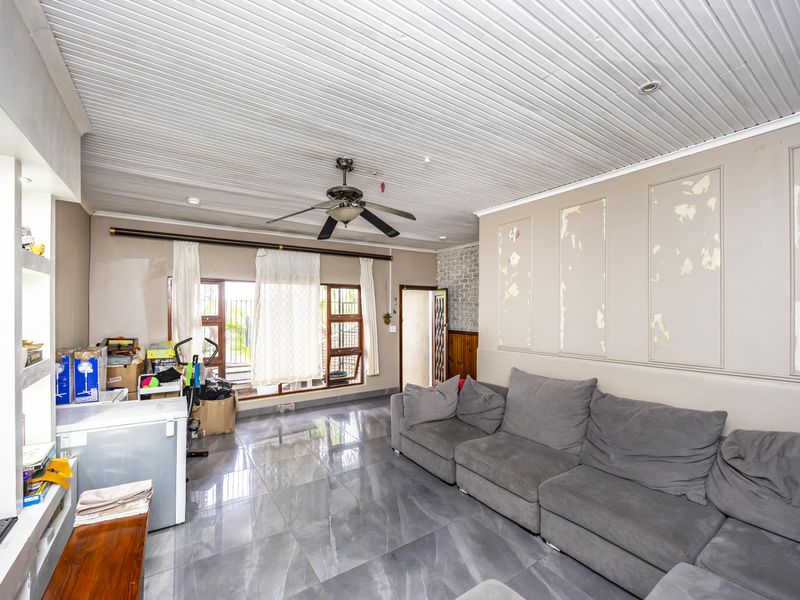 Living room featuring large format floor tiles, a ceiling fan, and timber-look ceiling panels, currently requiring cosmetic wall repairs and repainting.