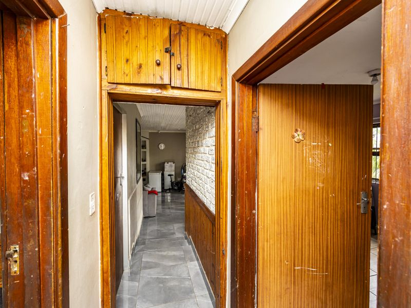 A narrow hallway featuring timber paneling, an exposed brick wall, tiled flooring, and built-in overhead storage cabinetry.