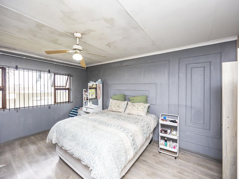 A bedroom featuring laminate flooring, a ceiling fan, and security bars on the windows, with visible water damage on the ceiling requiring repair.