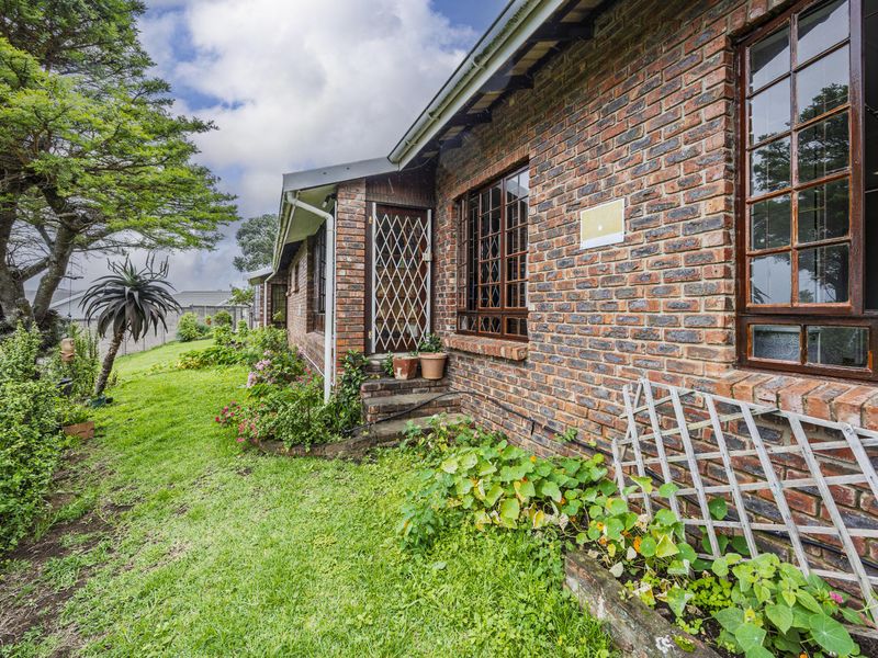 A view of the rear exterior of the townhouse featuring face brick walls, timber framed windows, and a well-maintained garden area.