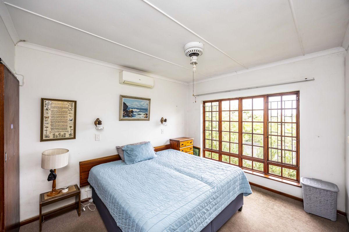 A bedroom featuring timber-framed windows with security bars, a ceiling fan, and a wall-mounted split system air conditioner.