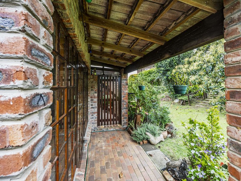 A covered patio area featuring exposed brick pillars, timber rafters, and clay roof tiles, providing access to the garden through a timber gate.