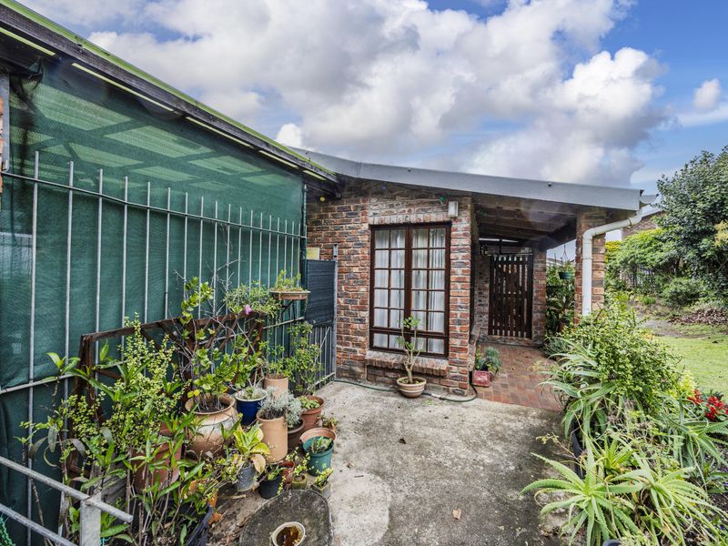 Rear exterior view of the townhouse featuring a face brick facade, a covered patio area, and a paved walkway leading to the garden.