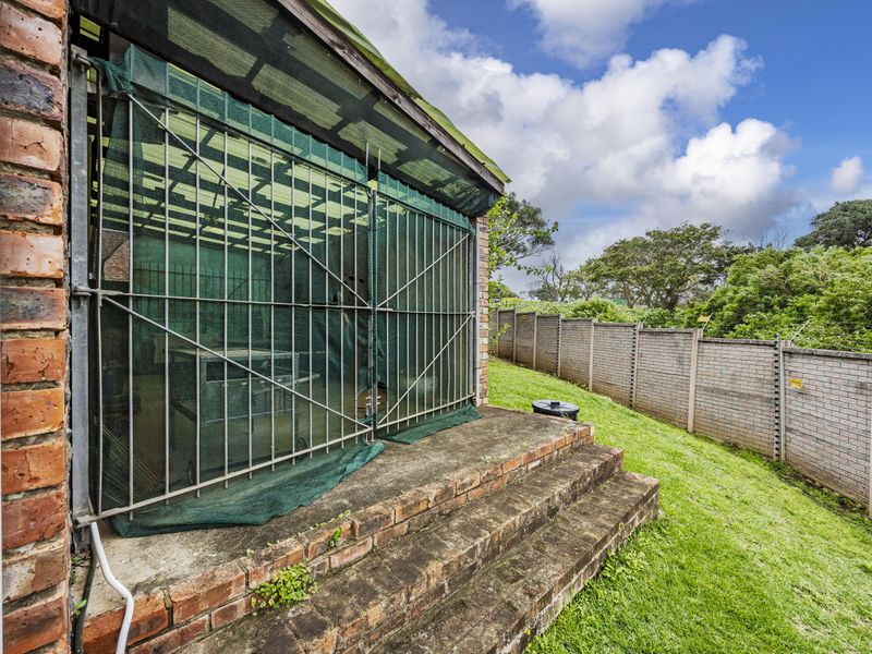 Rear exterior view of the townhouse featuring a brick-stepped patio area, enclosed with security gates and netting, overlooking a private garden and boundary wall.
