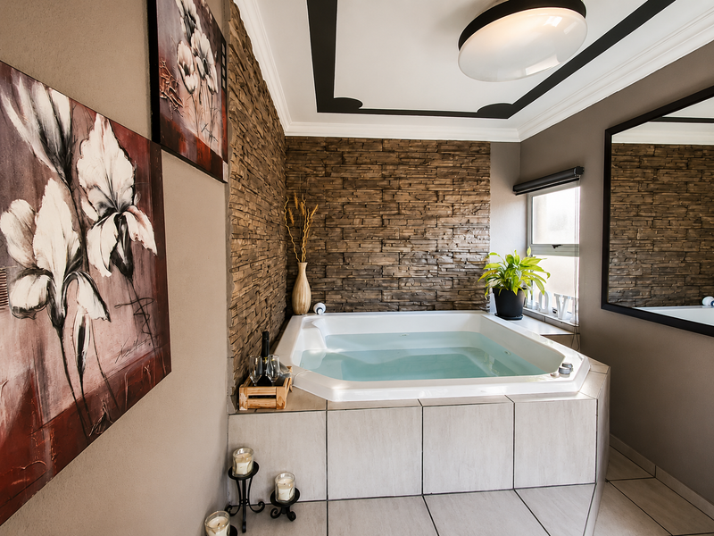 A well-maintained bathroom featuring a built-in corner bathtub, a decorative stone veneer feature wall, and large wall mirror.