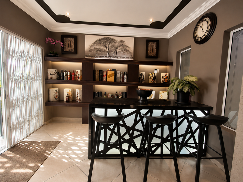 A well-appointed home bar featuring a modern illuminated counter, custom built-in shelving with integrated lighting, and decorative ceiling molding.