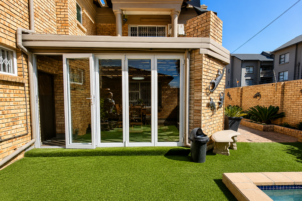 Rear exterior view featuring a face brick facade, bi-fold glass doors leading to an artificial lawn, and a swimming pool area.