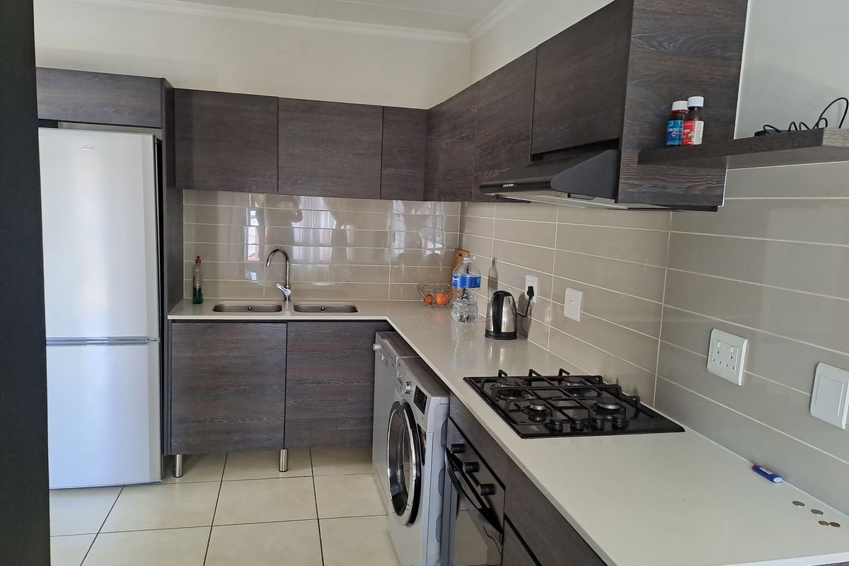 Modern kitchen featuring dark wood-grain cabinetry, stone countertops, integrated gas hob, oven, extractor fan, and tiled backsplash with neutral floor tiles.