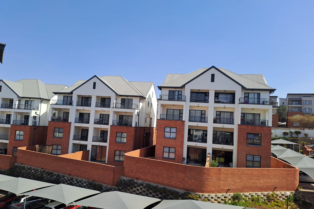 A view of the rear facade of a multi-story townhouse complex featuring brick and plaster finishes, private balconies, and covered parking bays.