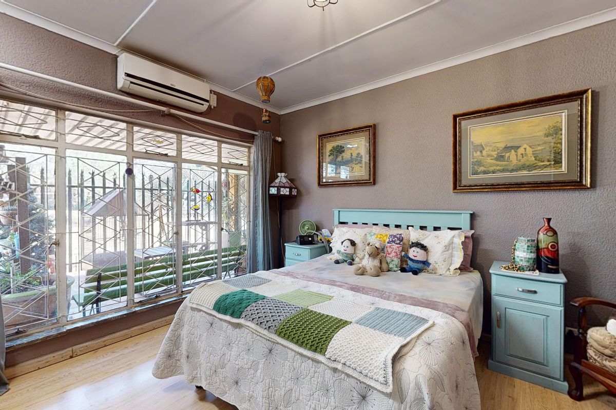 A bedroom featuring laminated flooring, an air conditioning unit, and large windows with security gates, offering direct access to the outdoor area.
