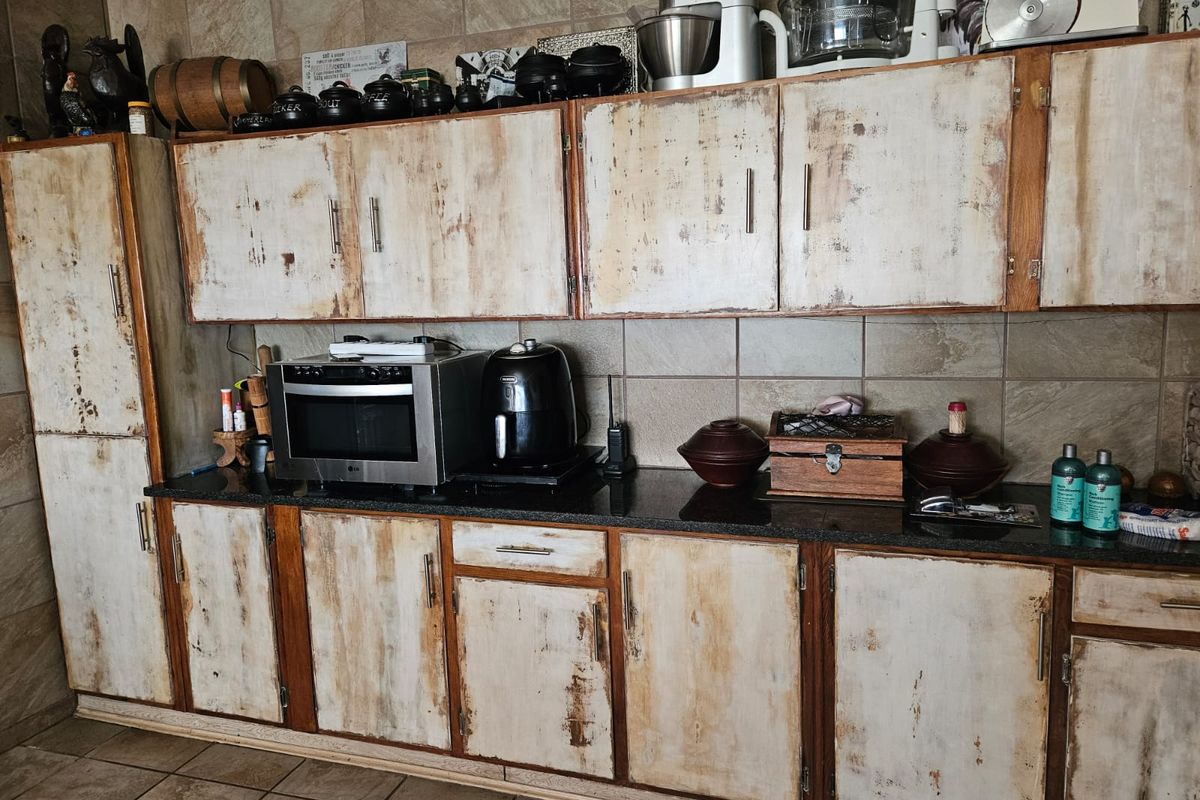 Kitchen featuring granite countertops, tiled backsplash, and distressed-finish cabinetry. The space offers functional storage and workspace, though the cabinetry shows significant wear.