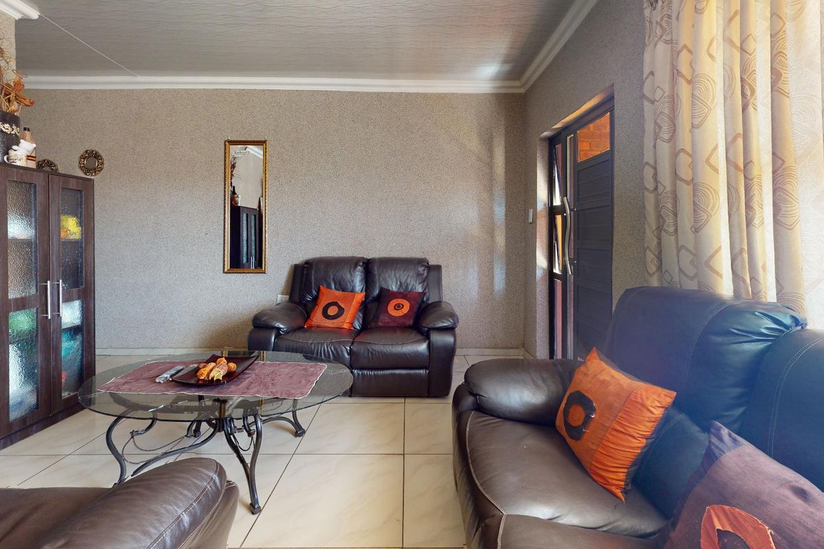 A comfortable living room featuring tiled flooring, textured wall finishes, and a glass-panelled exterior door providing natural light.