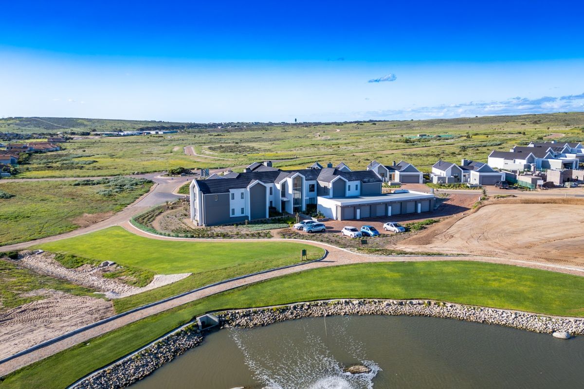 Aerial view of a modern residential apartment complex featuring landscaped grounds, a water feature, and paved access roads in a scenic estate setting.