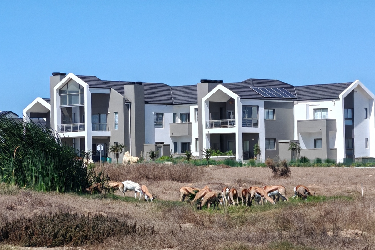 A modern apartment complex featuring contemporary architectural design, tiled roofing, solar panels, and private balconies, set against a natural landscape.
