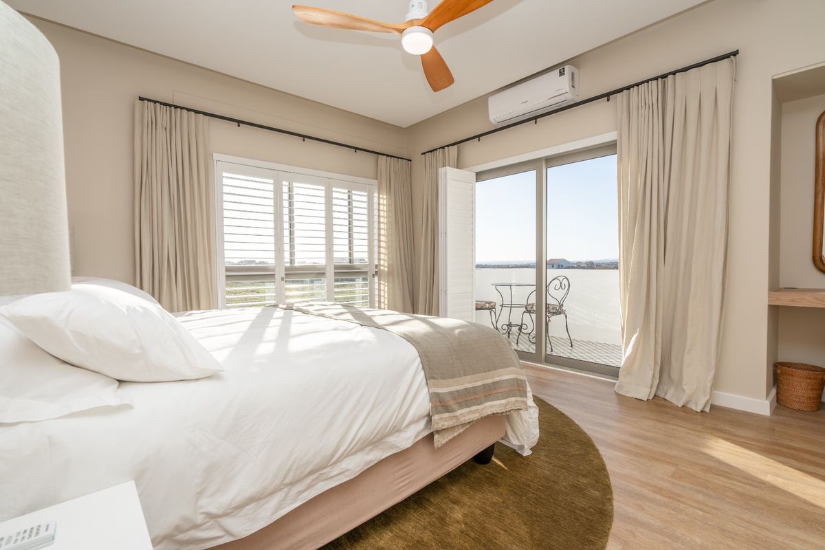 Bright bedroom featuring laminate flooring, a ceiling fan, split-system air conditioning, and direct access to a private balcony through sliding glass doors.