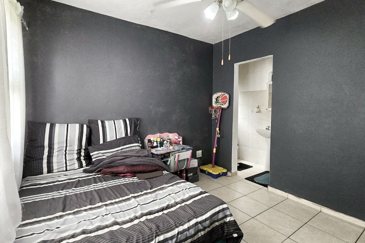A bedroom featuring dark painted walls, tiled flooring, and an integrated ceiling fan, with direct access to an en-suite bathroom.