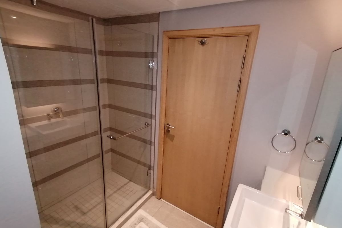 A modern bathroom featuring a glass-enclosed shower with horizontal tiled accents, a wall-mounted basin, and a timber door.