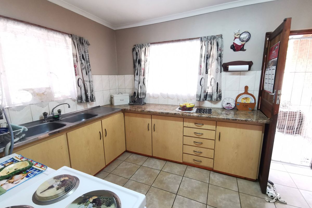 Functional kitchen featuring light wood cabinetry, laminate countertops, double basin sink, and tiled flooring with direct access to an exterior area.