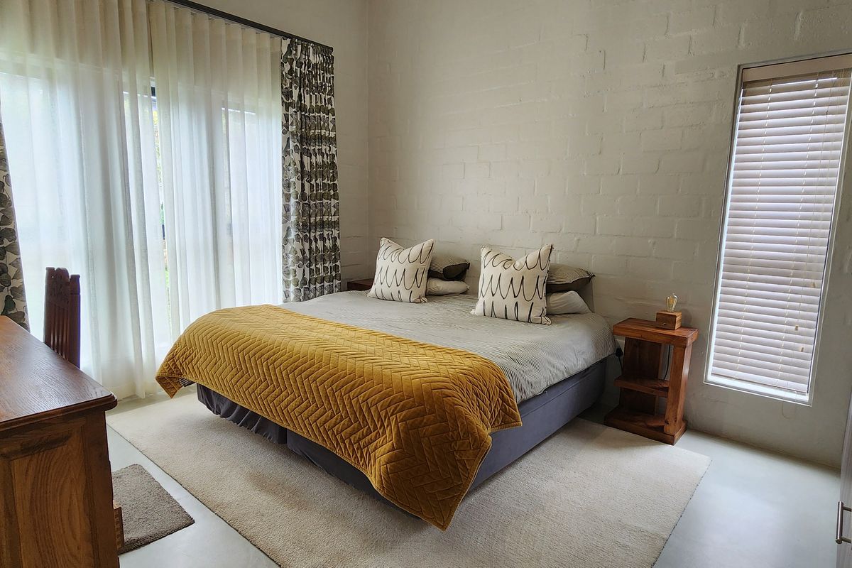 A well-lit bedroom featuring painted brick walls, large sliding glass doors with curtains, and a vertical window with fitted blinds.