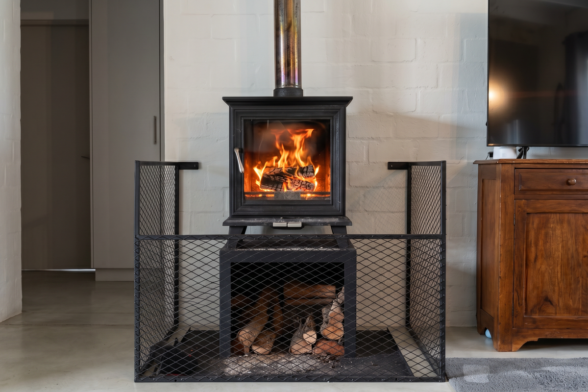 A cozy living area featuring a modern black wood-burning fireplace with a protective metal screen and a polished concrete floor.