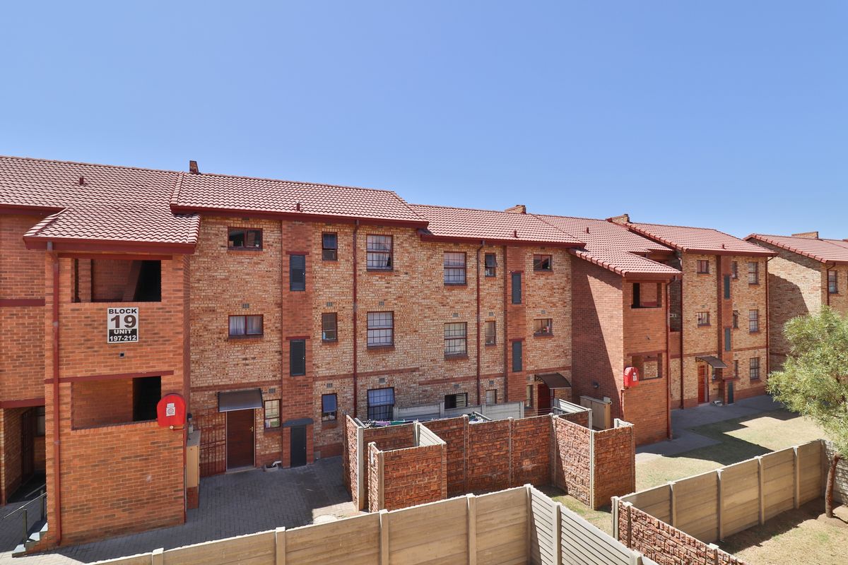 Exterior view of a multi-story brick apartment block featuring tiled roofing, paved ground-level courtyards, and enclosed private outdoor spaces.