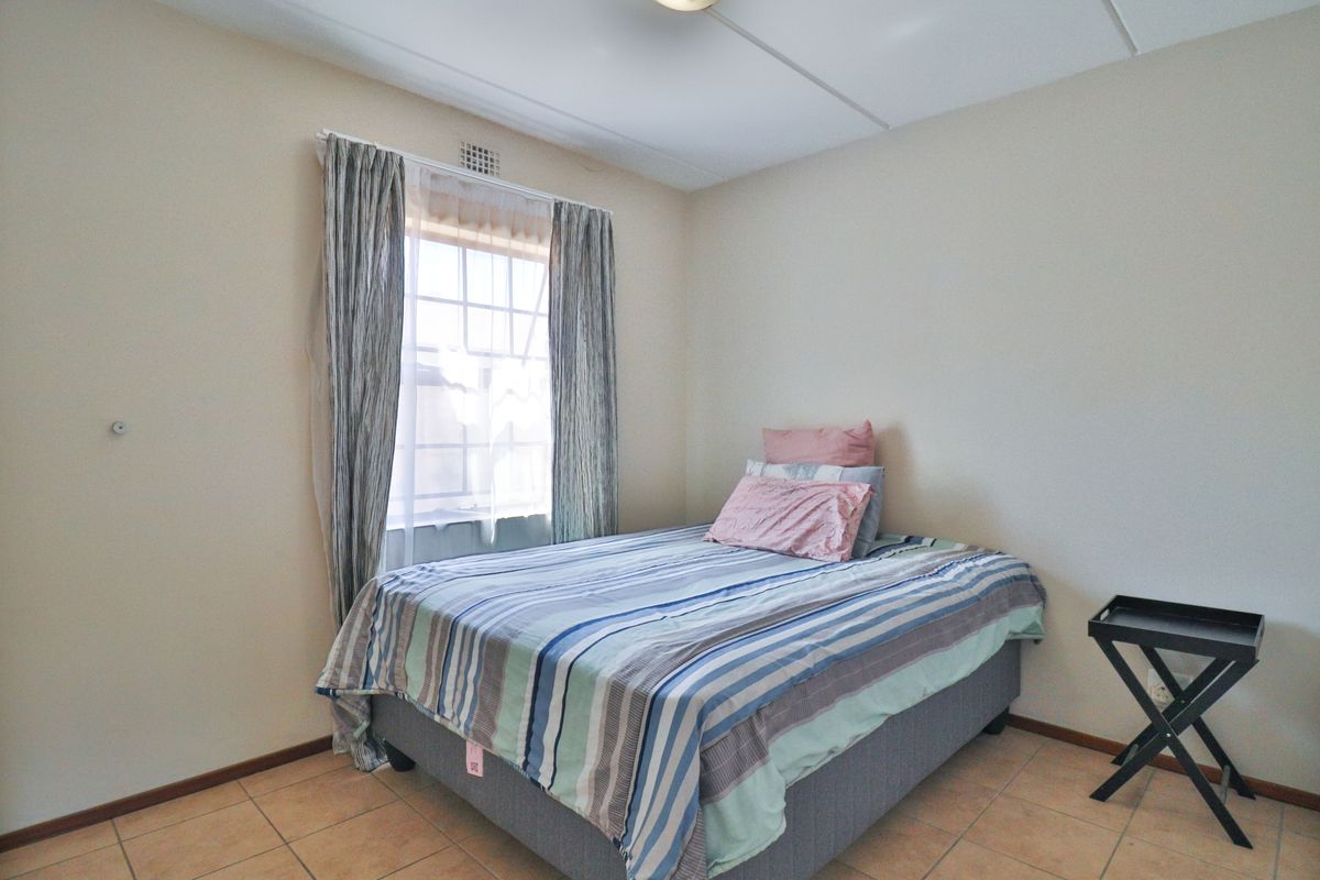 A simple bedroom featuring tiled flooring and a window with curtains, providing a functional and neutral living space.