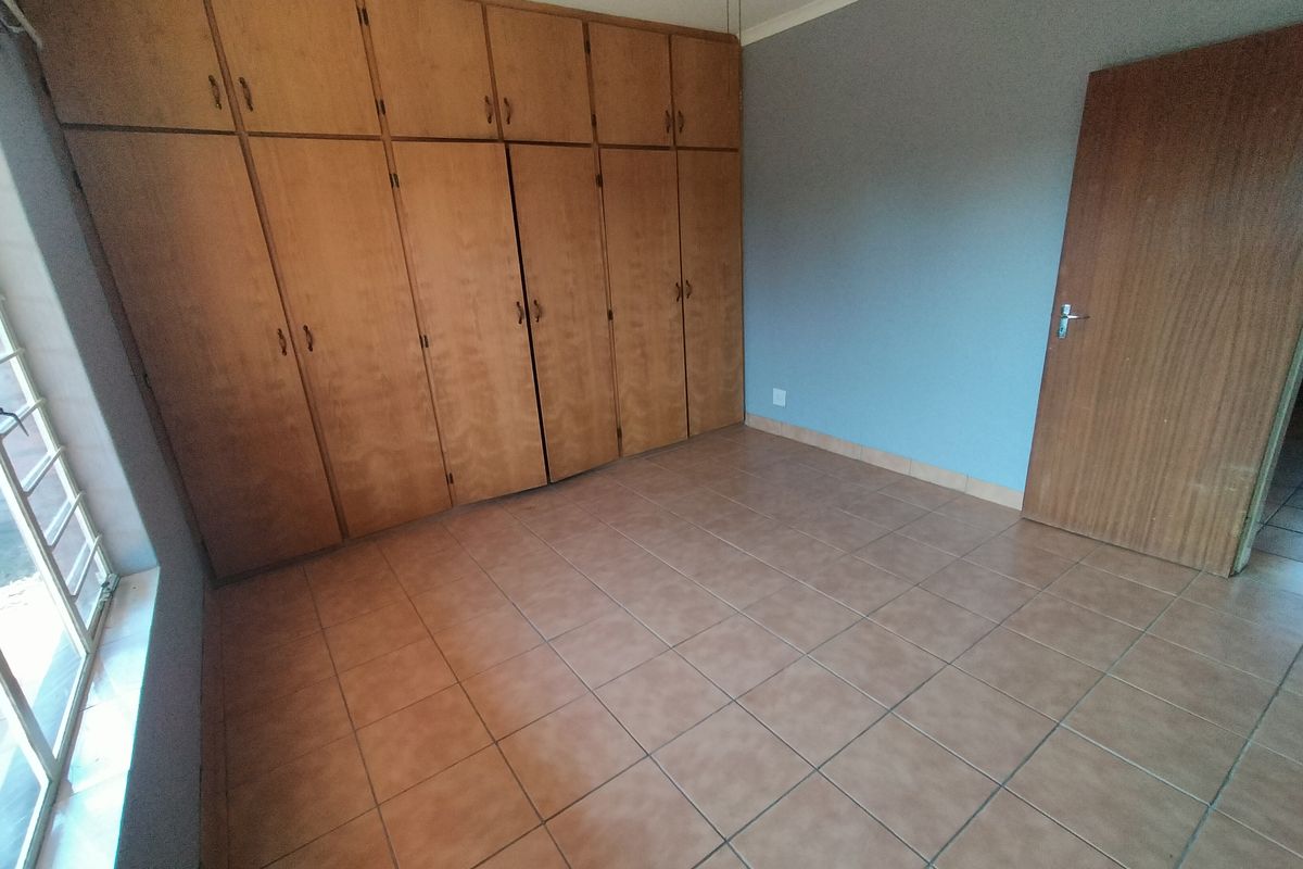 An empty bedroom featuring tiled flooring and extensive built-in wooden cupboards, providing ample storage space.