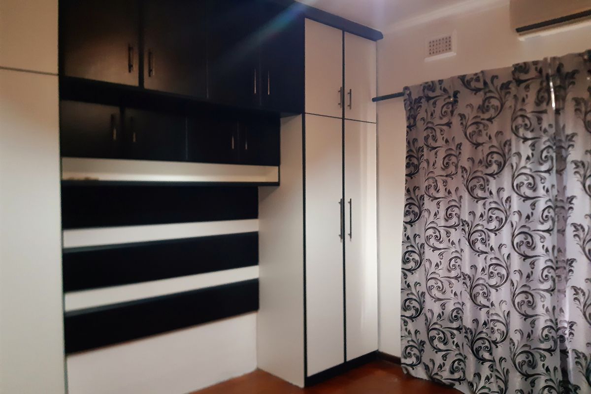Bedroom featuring built-in cabinetry with overhead storage and a tall wardrobe unit, complemented by wooden flooring.