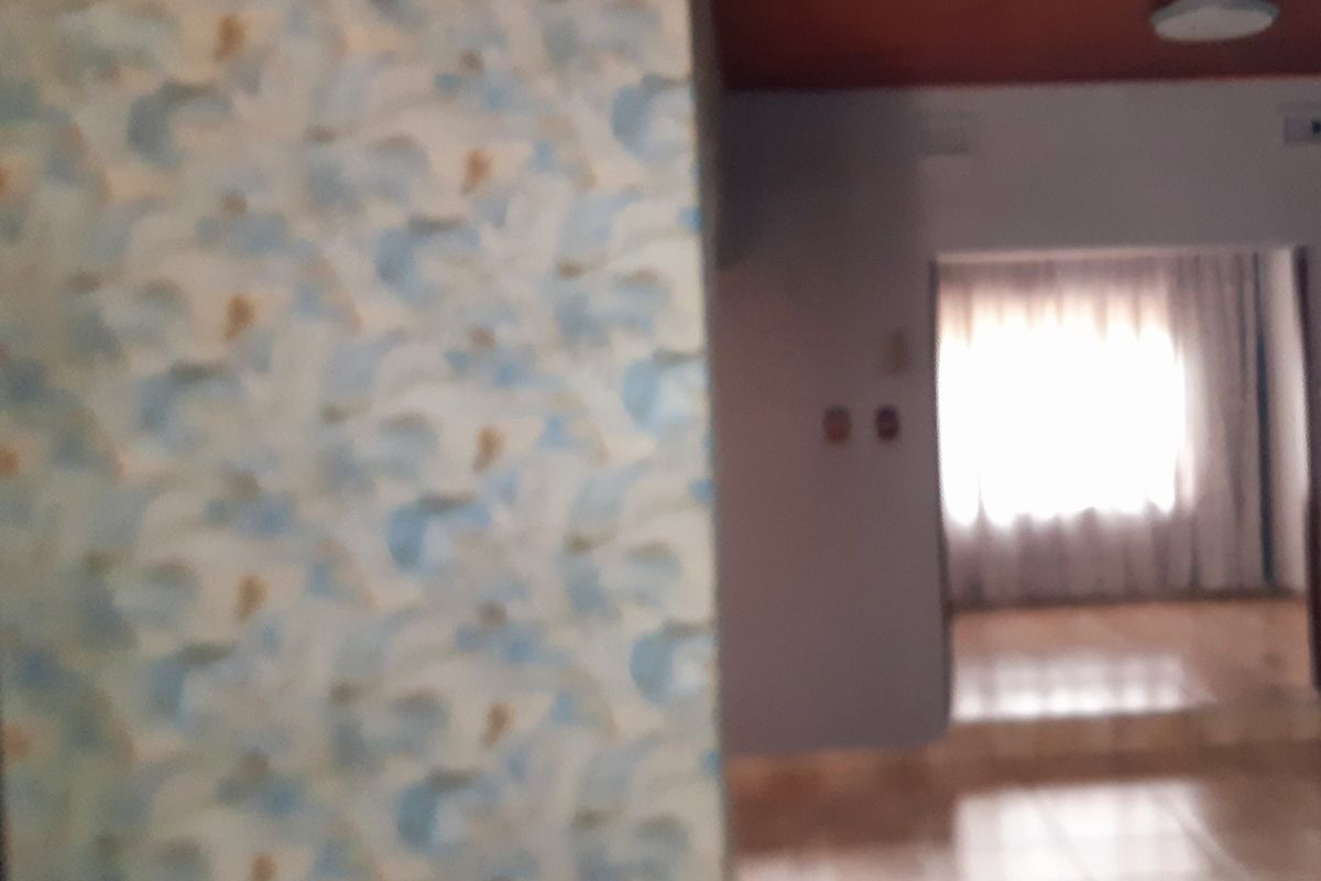 Interior view of a living area featuring patterned wallpaper, a wooden ceiling, and tiled flooring leading to an adjacent room.