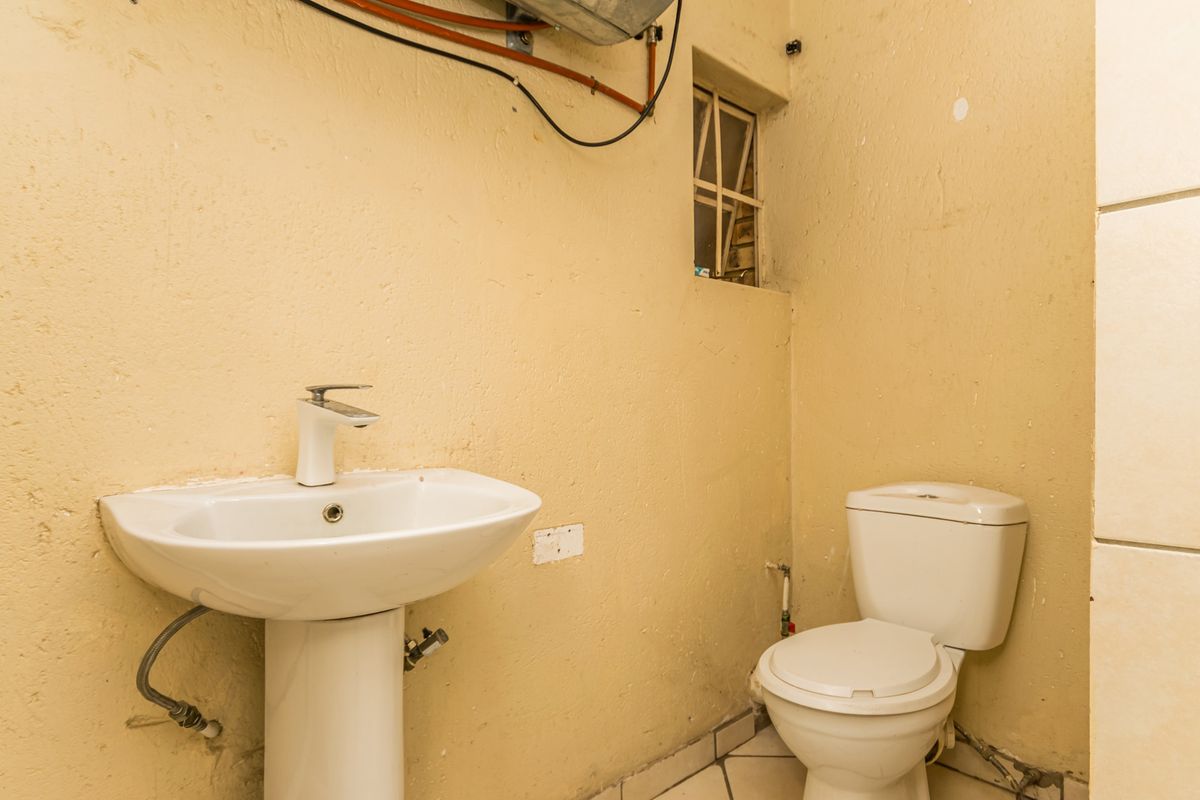 A small, basic bathroom featuring a pedestal basin and toilet, requiring cosmetic updates and finish repairs to improve the overall condition.