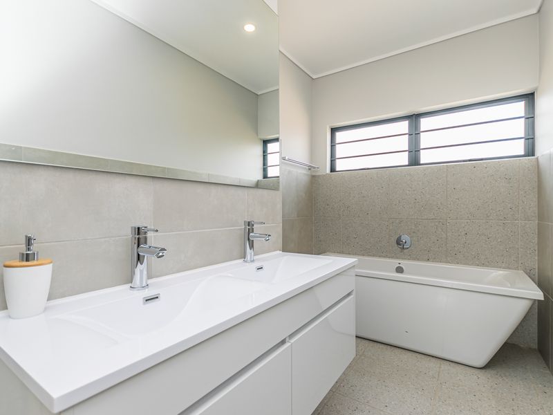 Modern bathroom featuring a sleek double vanity, a contemporary freestanding bathtub, large wall-mounted mirror, and neutral tiled finishes throughout.