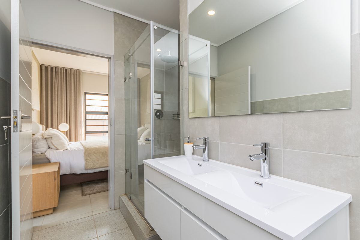 Modern bathroom featuring a double vanity with integrated sinks, a glass-enclosed shower with a rain shower head, and neutral wall and floor tiling.