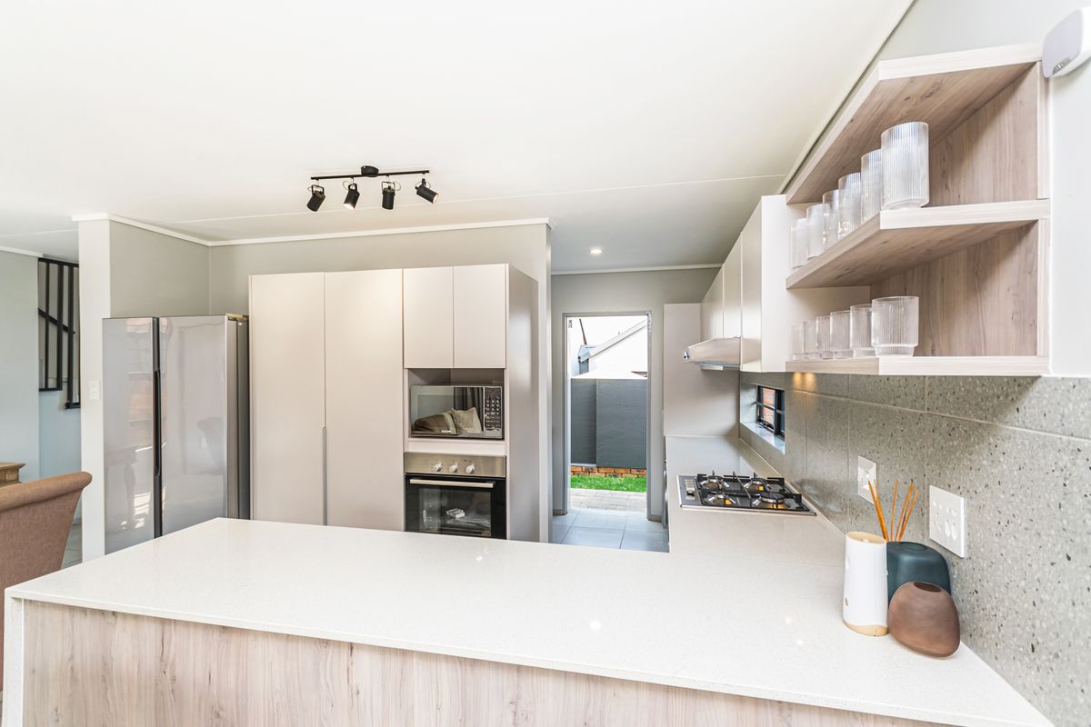 Modern kitchen featuring stone countertops, built-in oven, gas hob, extractor fan, and sleek cabinetry with open shelving, leading to an outdoor area.