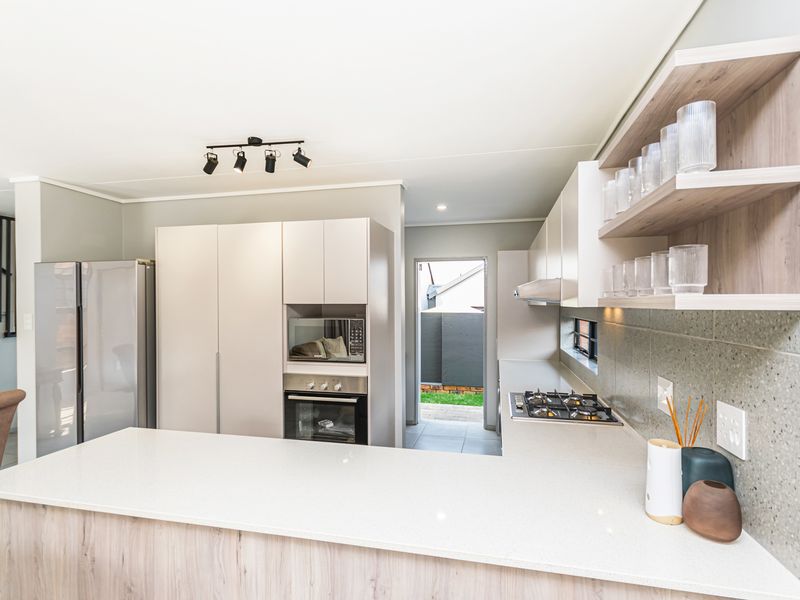 Modern kitchen featuring stone countertops, built-in oven, gas hob, extractor fan, and sleek cabinetry with open shelving, leading to an outdoor area.