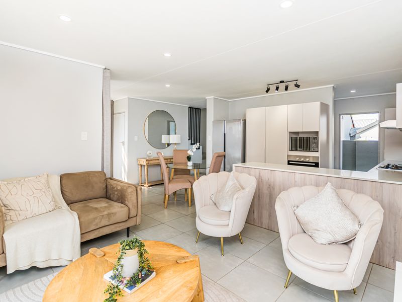 Modern open-plan living area featuring a contemporary kitchen with integrated appliances, sleek cabinetry, and tiled flooring, seamlessly flowing into the dining and lounge space.