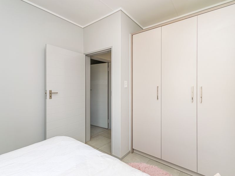 A clean, well-maintained bedroom featuring neutral walls, built-in wardrobes with modern handles, and a functional internal door leading to an adjacent space.