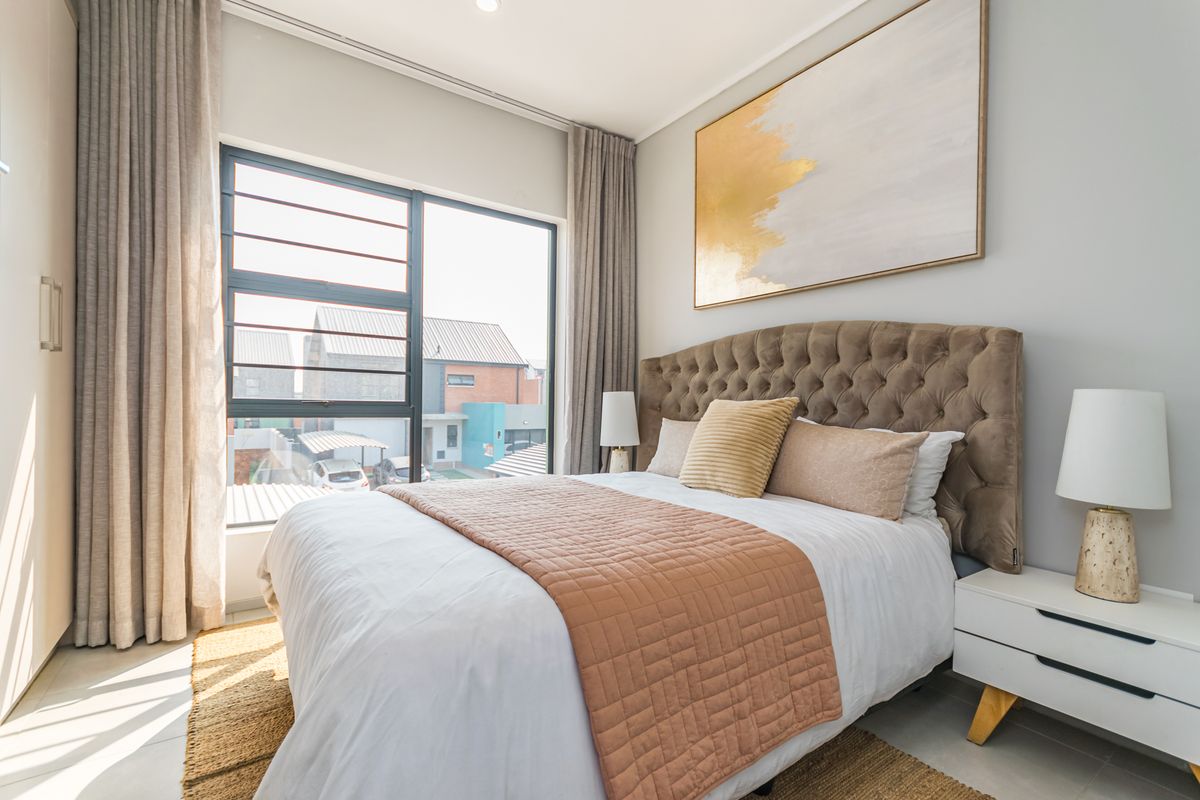 A well-lit, modern bedroom featuring a built-in wardrobe, neutral finishes, and large aluminium-framed windows providing natural light.
