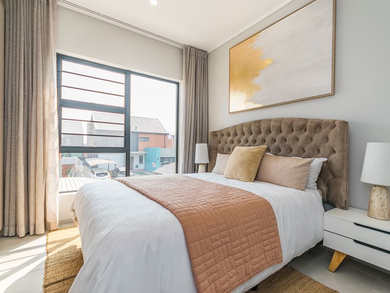 A well-lit, modern bedroom featuring a built-in wardrobe, neutral finishes, and large aluminium-framed windows providing natural light.
