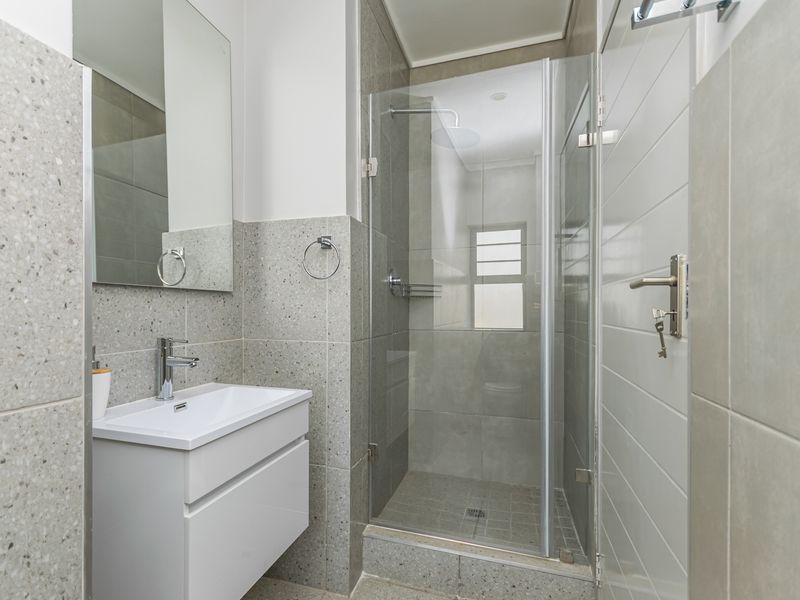 Modern bathroom featuring a sleek vanity cabinet, wall-mounted mirror, and a glass-enclosed shower with contemporary grey tiling throughout.