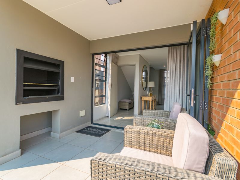 Covered patio featuring a built-in braai, tiled flooring, and large sliding doors providing seamless access to the interior living space.