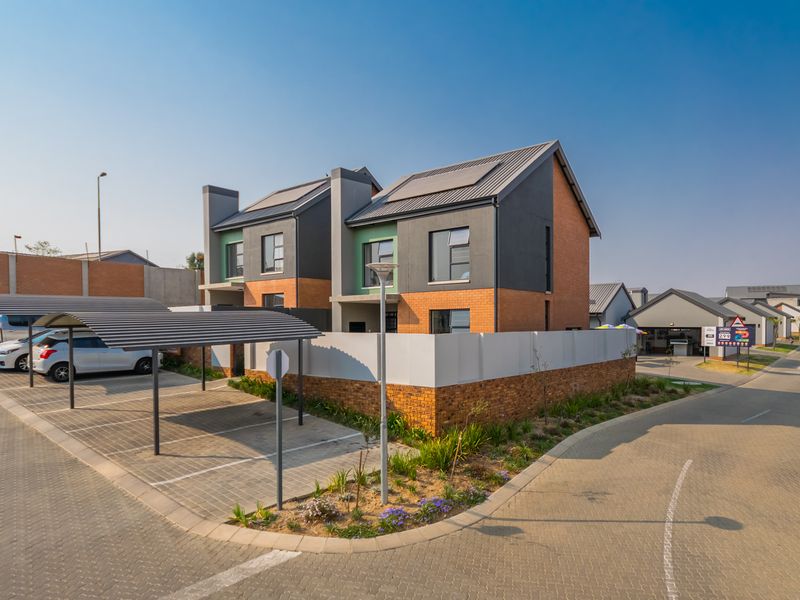 Modern townhouse exterior featuring a brick and dark render facade, solar panels, and a dedicated paved carport area within a secure complex.