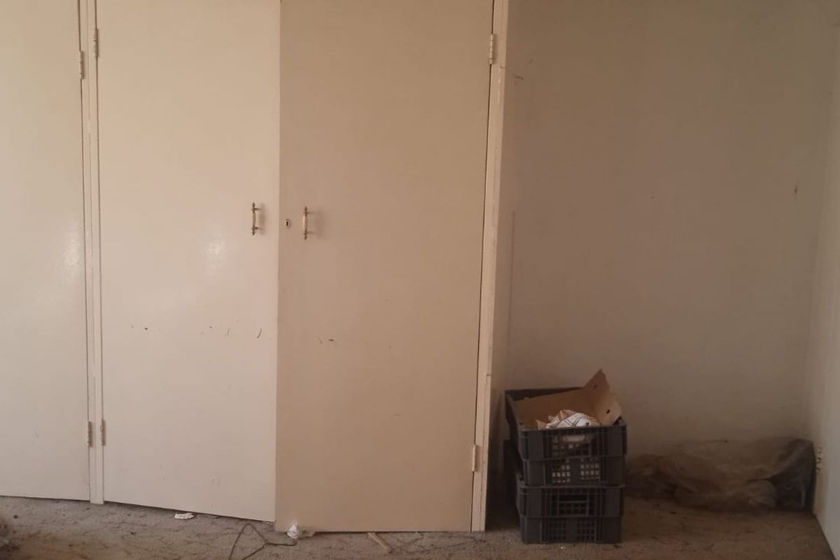 A bedroom interior featuring built-in storage cupboards with dated finishes and plain wall surfaces, requiring cosmetic updates.